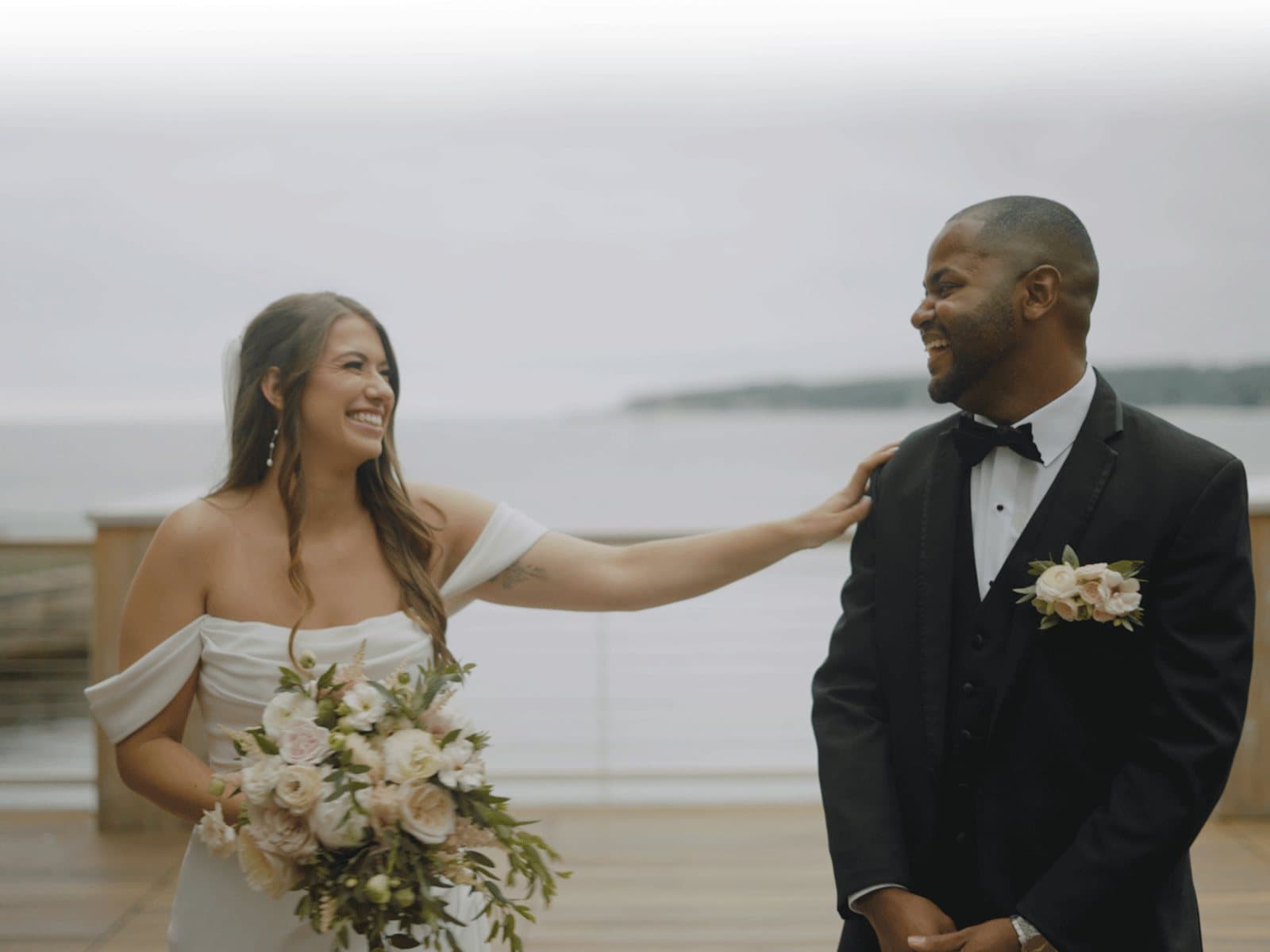 A graded Skytona film still of a couple laughing on an oceanfront deck.